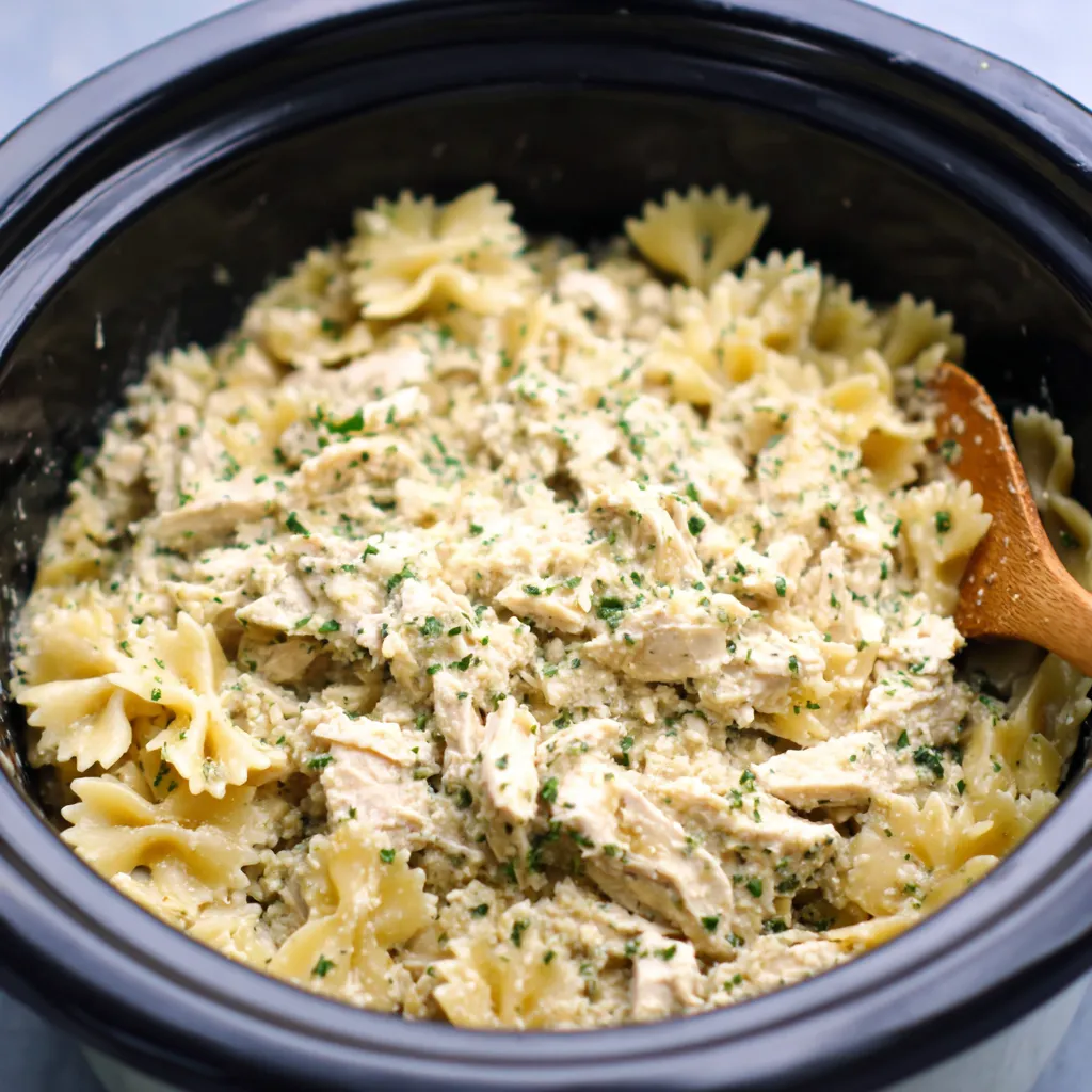 Creamy Crockpot Garlic Parmesan Chicken Pasta is shown prepared in a slow cooker, ready to serve.
